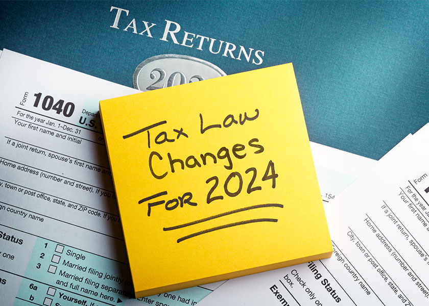 A yellow note pad rests on top of a 1040 tax form with a reminder of the new tax laws to be implemented for 2024.