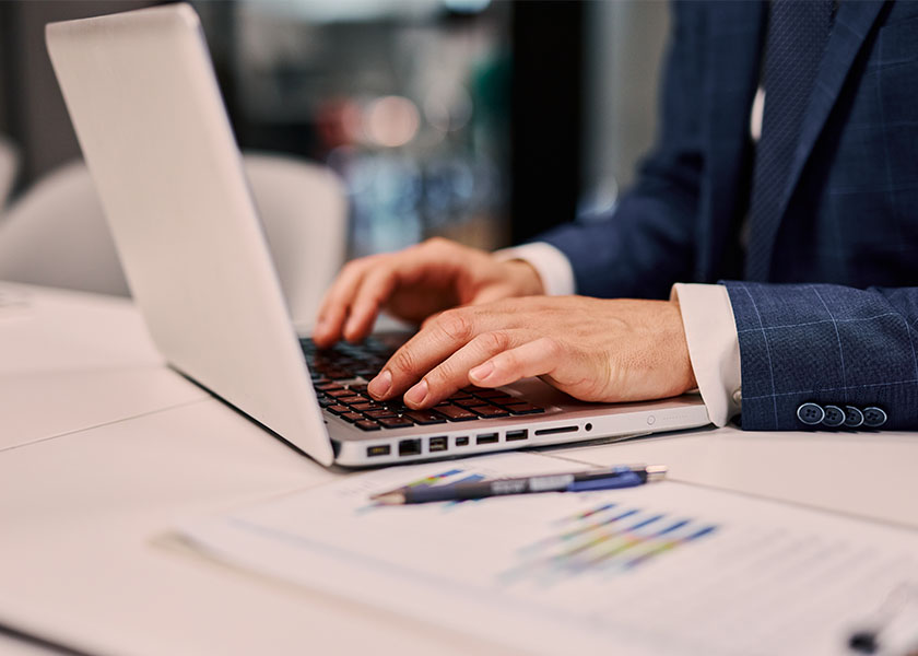 Close-up of a financial advisor's hands typing on a laptop keyboard while analyzing financial data and preparing a report in an office environment.